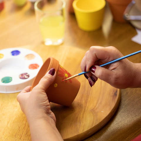 Women painting a flower pot at a wooden table