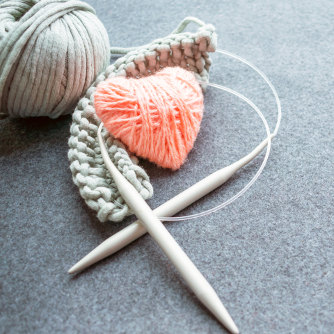 Knitting needles with gray yarn casted on and a pink yarn heart