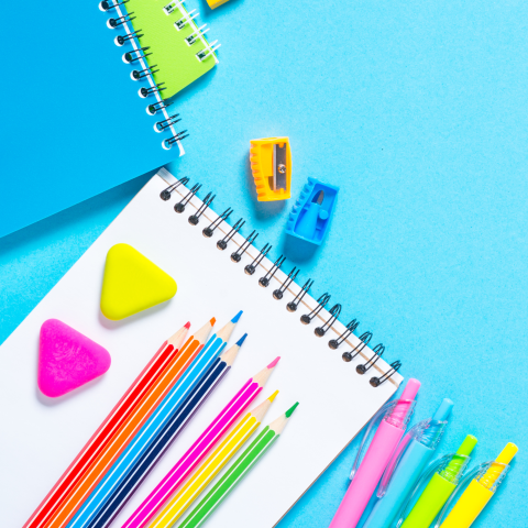 Photo of a notebook and colored pencils, pens, erasers and highlighters on a bright blue background