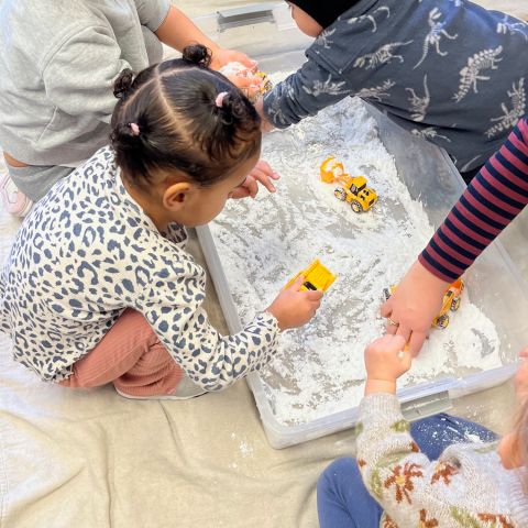 Image of a preschooler playing in a bin of white snowy material and toy trucks