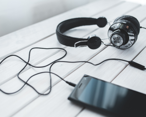 Headphones plugged into a cellphone, on top of a white surface